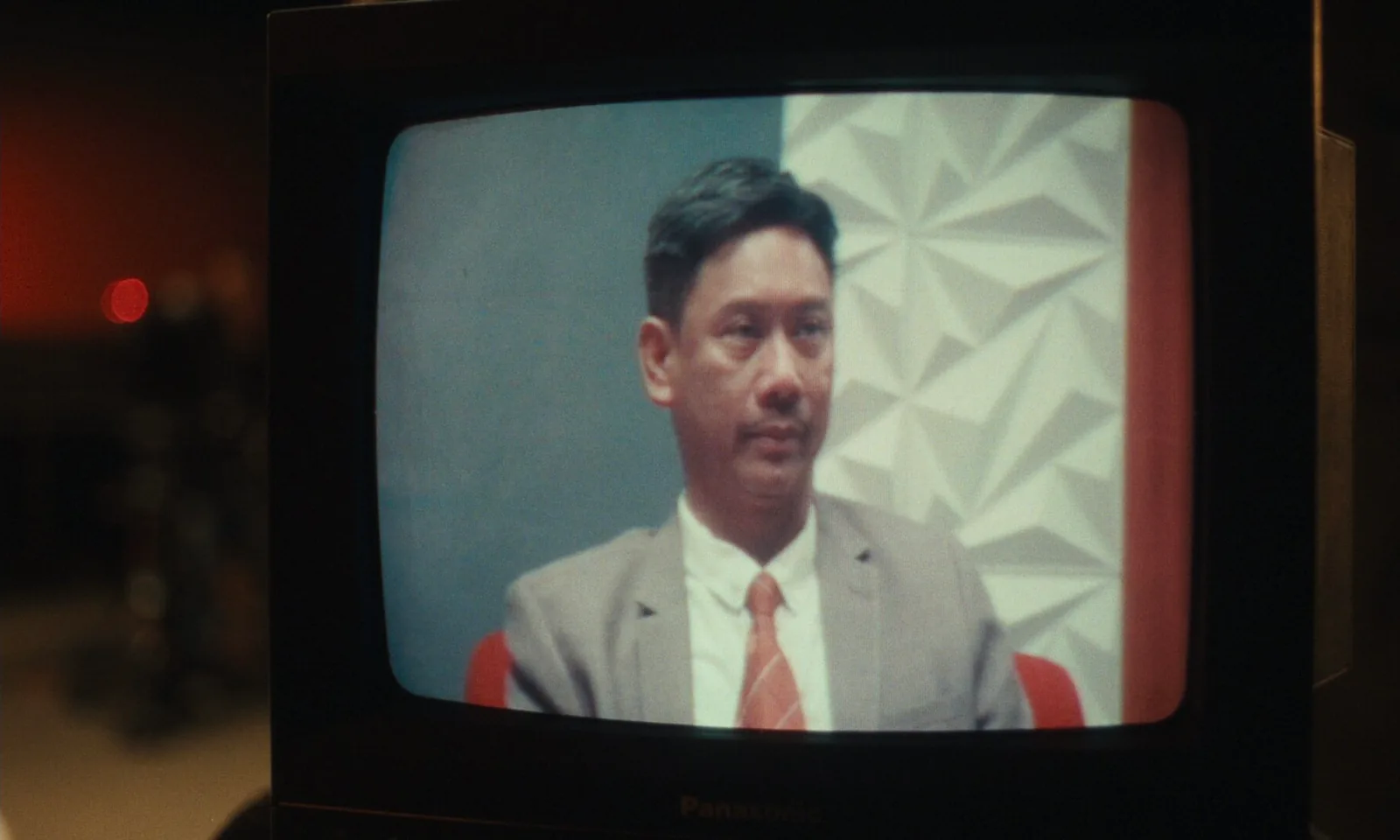 A man in a grey suit and orange tie on the screen of an old television set.